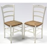 A pair of white painted wooden ladder-back kitchen chairs with woven rush seats, & on round
