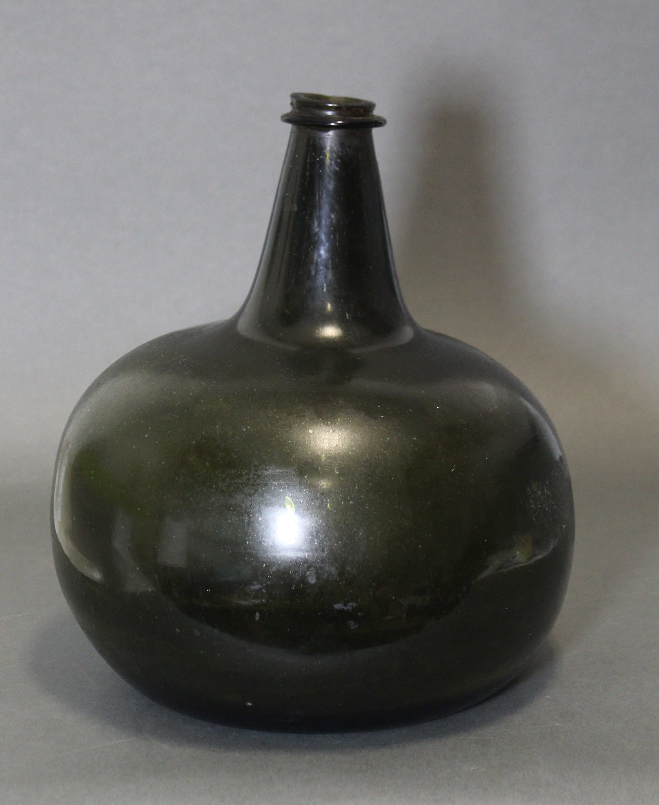 An 18th century green glass wine bottle of squat “onion” form, with tapered neck, 10¾” high. (slight