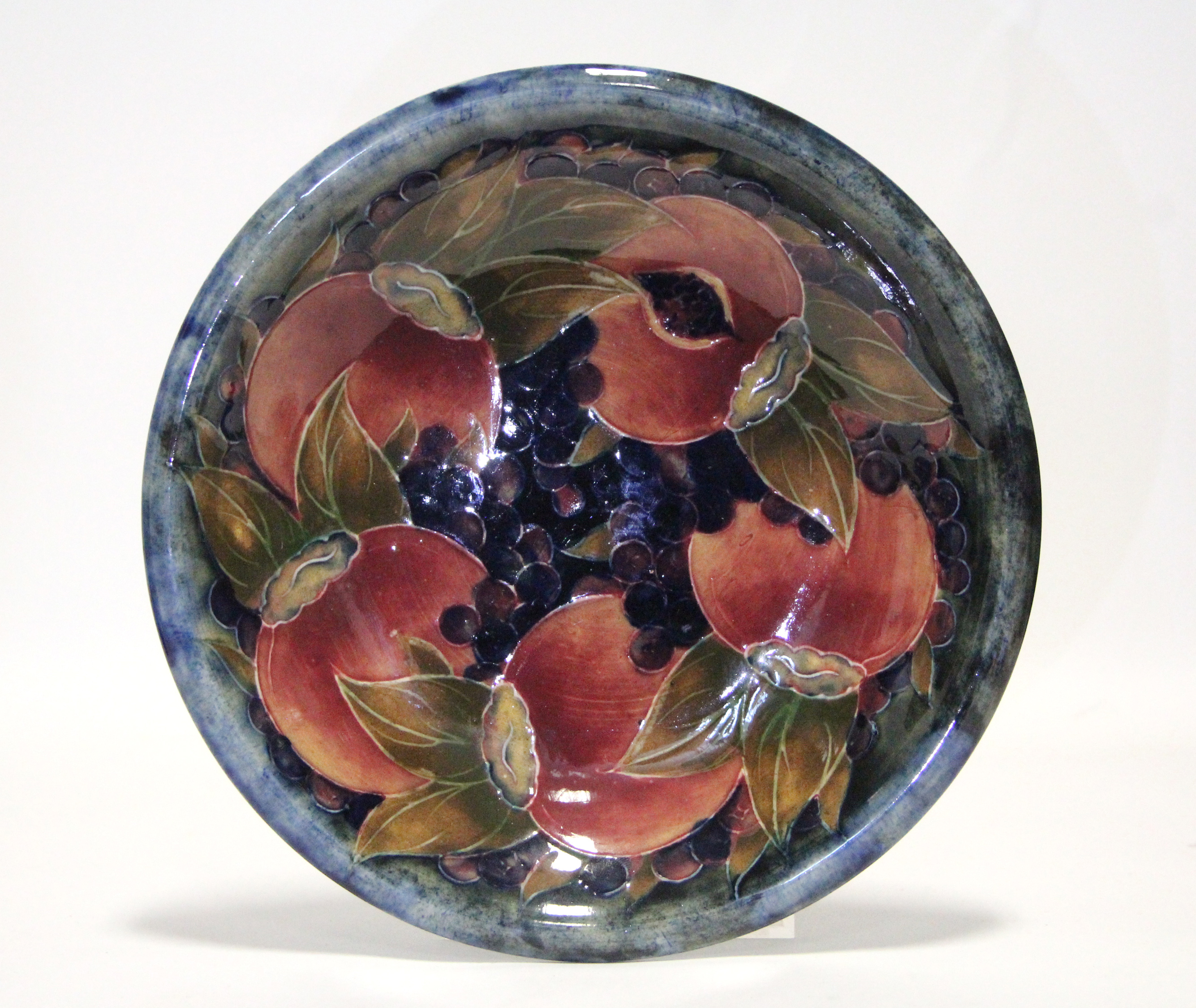 A Moorcroft “Pomegranate” circular shallow dish of mottled blue/green ground, painted initials &