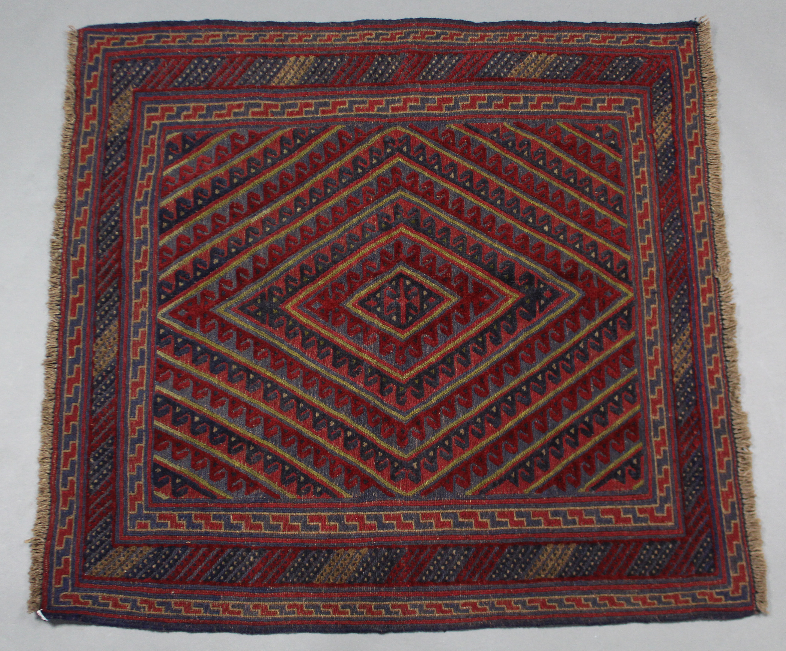 A Kazak rug of crimson, deep blue, & ivory ground with central hook & lozenge motif within