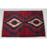 A Baluchi rug of crimson, deep blue, & ivory ground with two central lozenges in zig-zag borders;