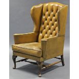 An 18th century style wing-back armchair, upholstered brass-studded tan leather, with buttoned back,