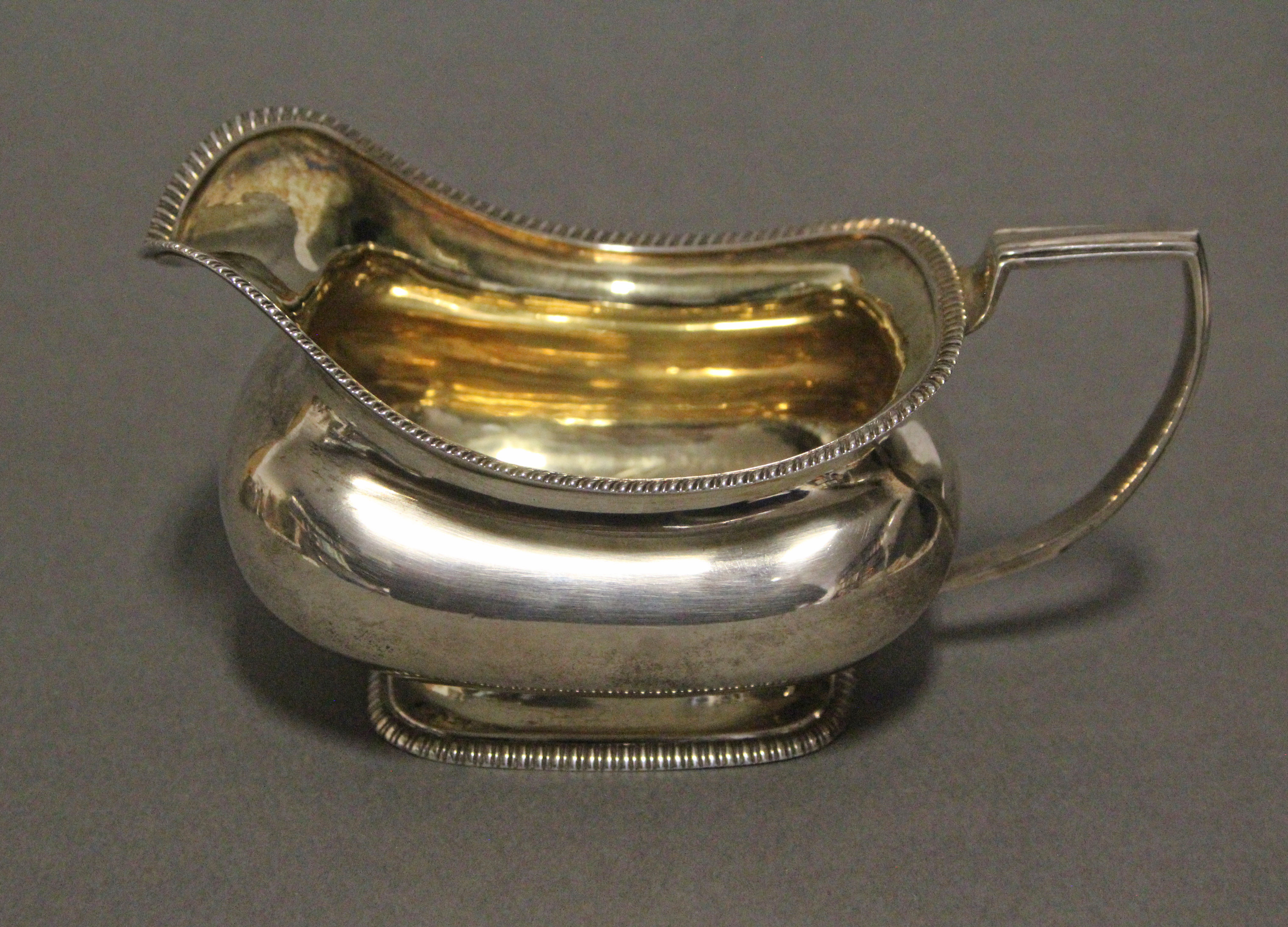 A regency silver cream jug of squat oblong form with gadrooned rims, reeded angular handle, & gilt