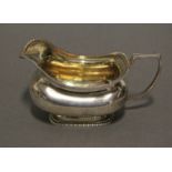 A regency silver cream jug of squat oblong form with gadrooned rims, reeded angular handle, & gilt