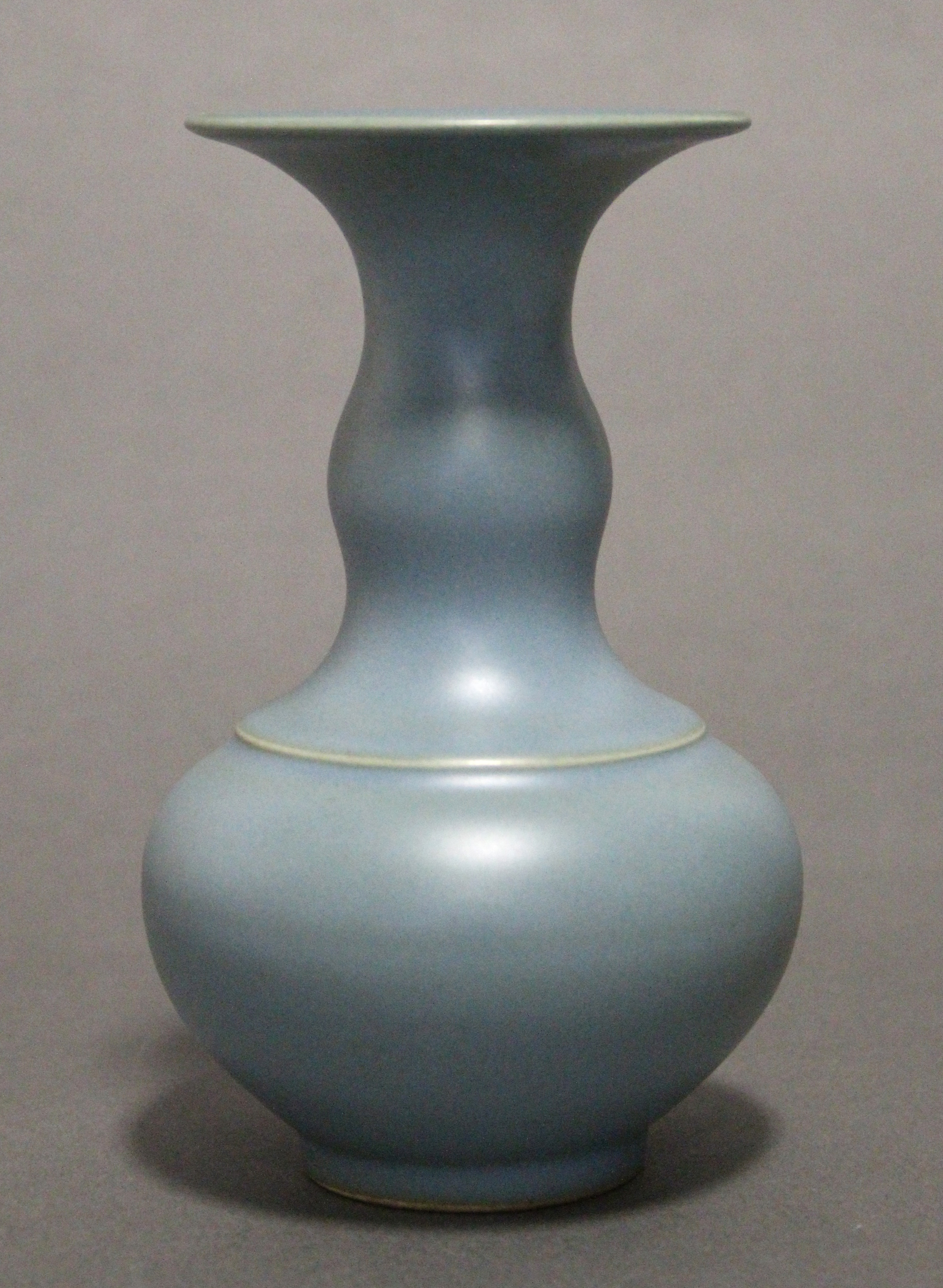 A Chinese pale blue glazed porcelain squat round vase with wide flat rim to the narrow neck, bears