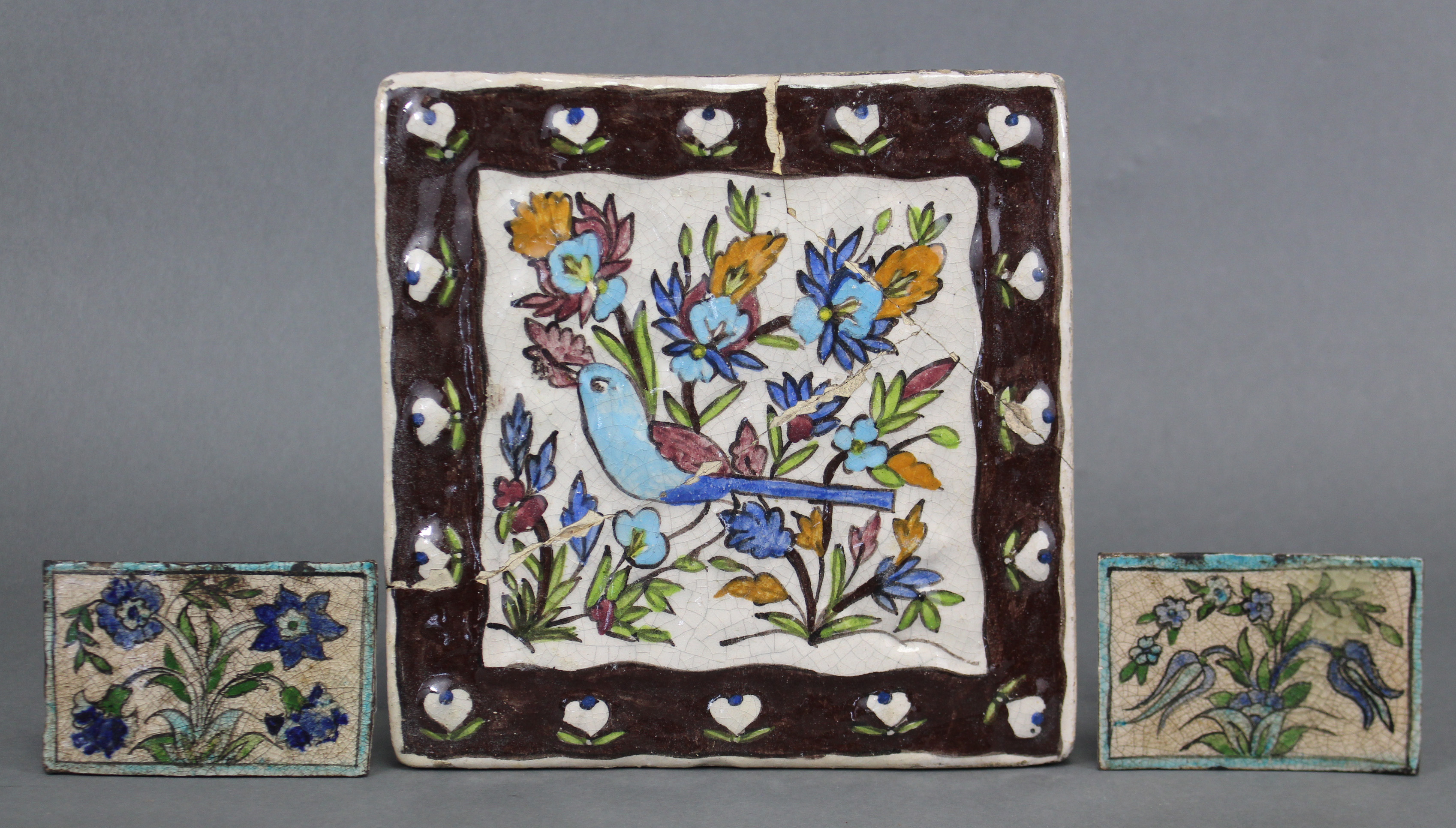 A Persian (?) pottery large square tile painted with a bird amongst flowers within a wide brown - Image 2 of 3