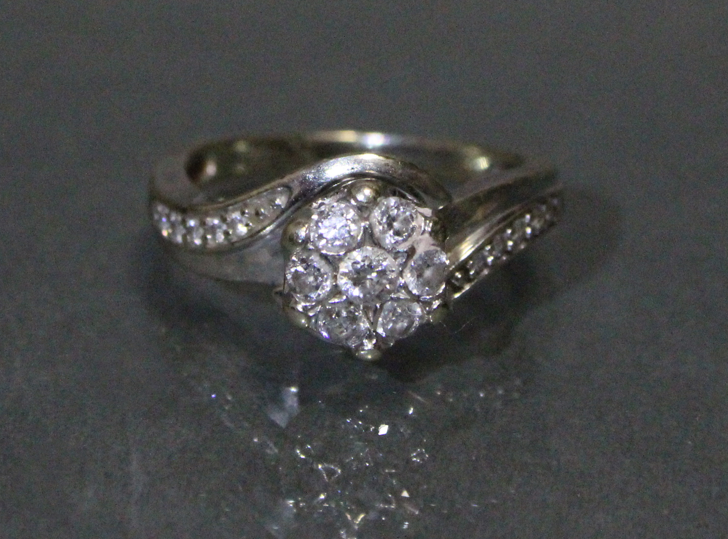 A diamond cluster ring set seven small stones, a row of five further stones to each curved shoulder,
