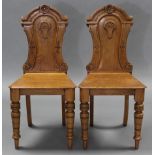 A pair of Victorian light oak hall chairs, each with carved decoration the shaped backs, hard