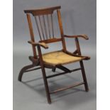 An Arts & Crafts style ash & elm folding elbow chair with spindle back, shaped arms & rush seat.