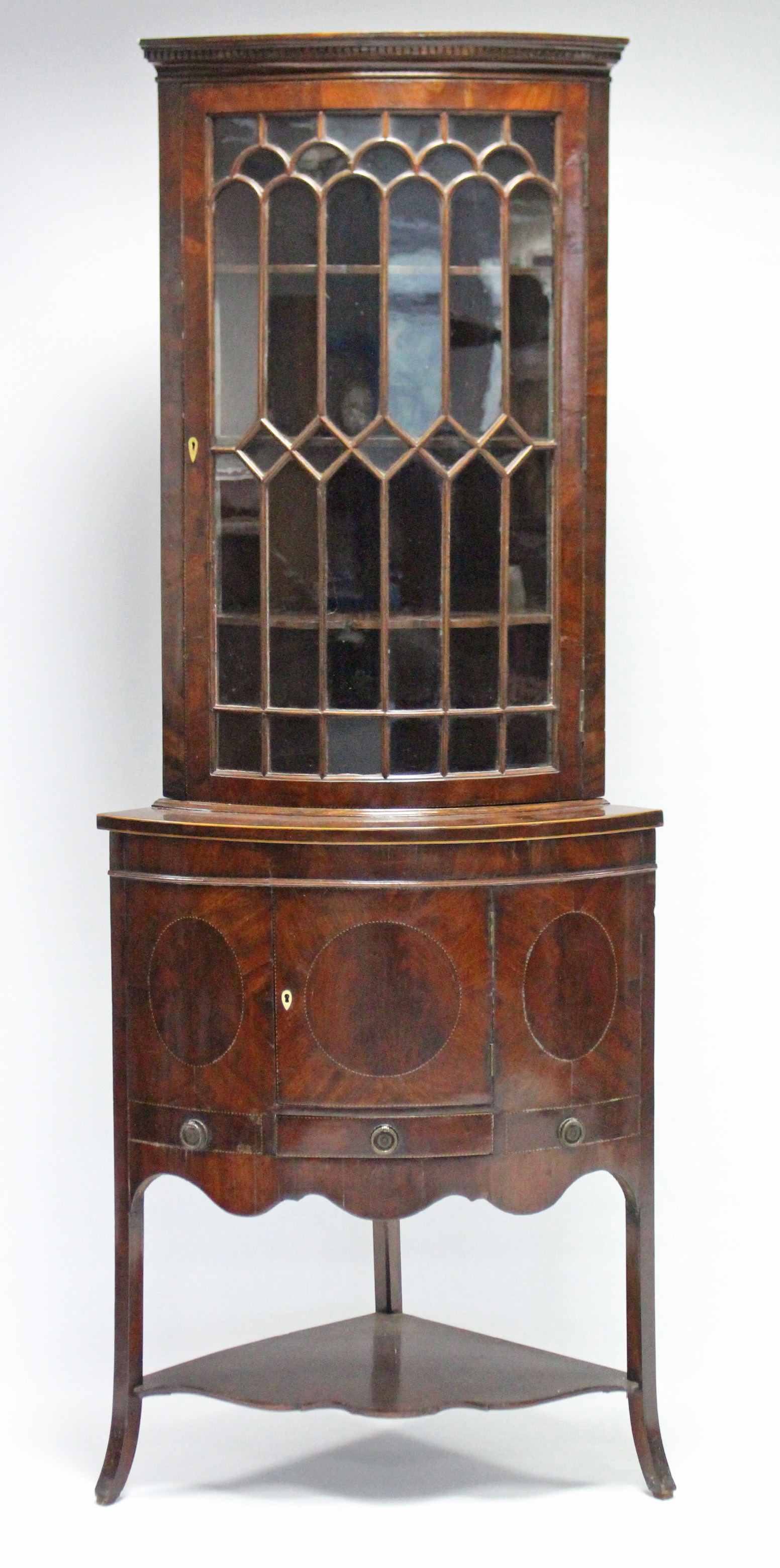 An early 19th century inlaid-mahogany standing corner cabinet, the upper part fitted three shaped