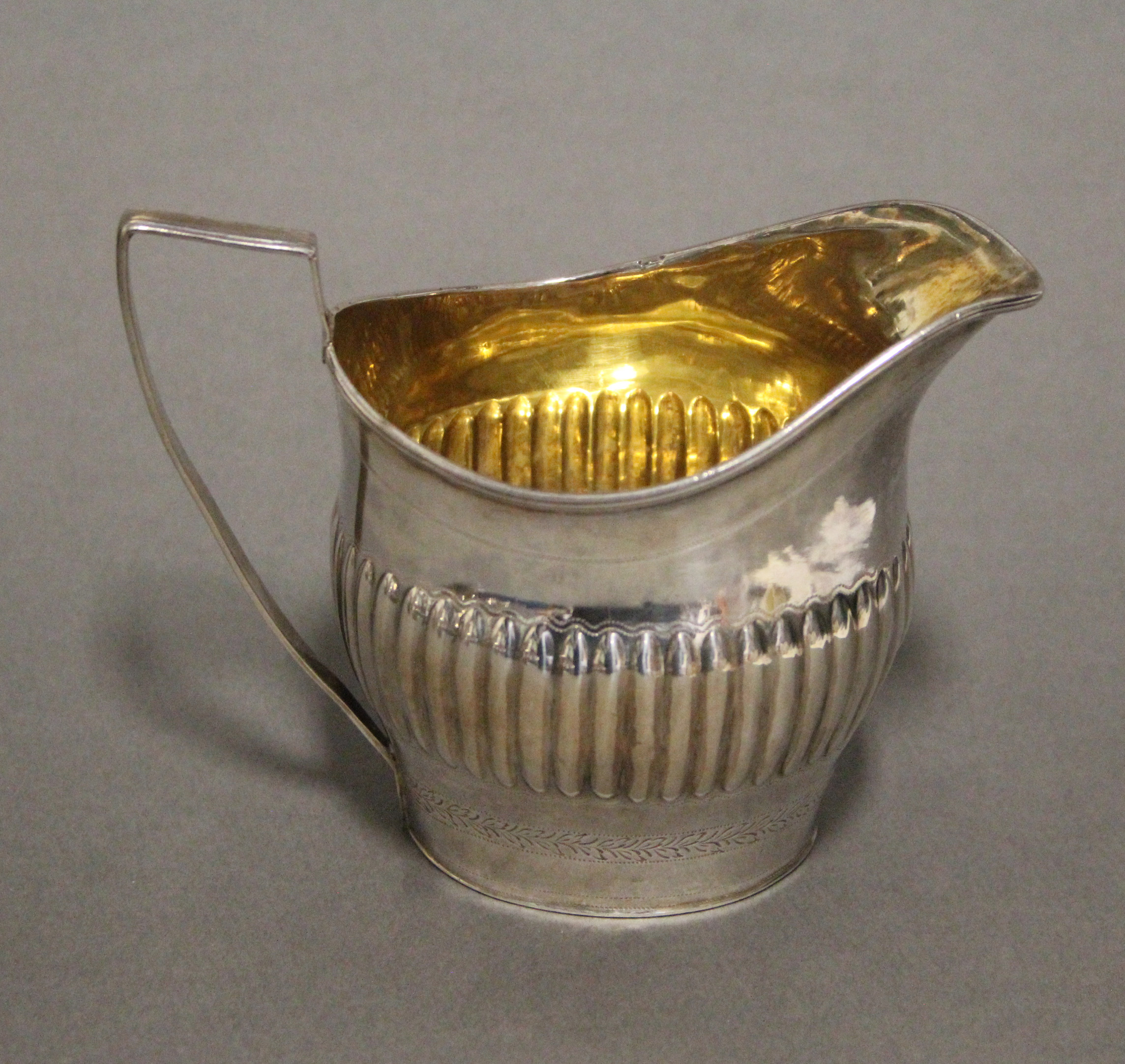A George III silver oval semi-fluted cream jug with engraved foliate band, reeded angular