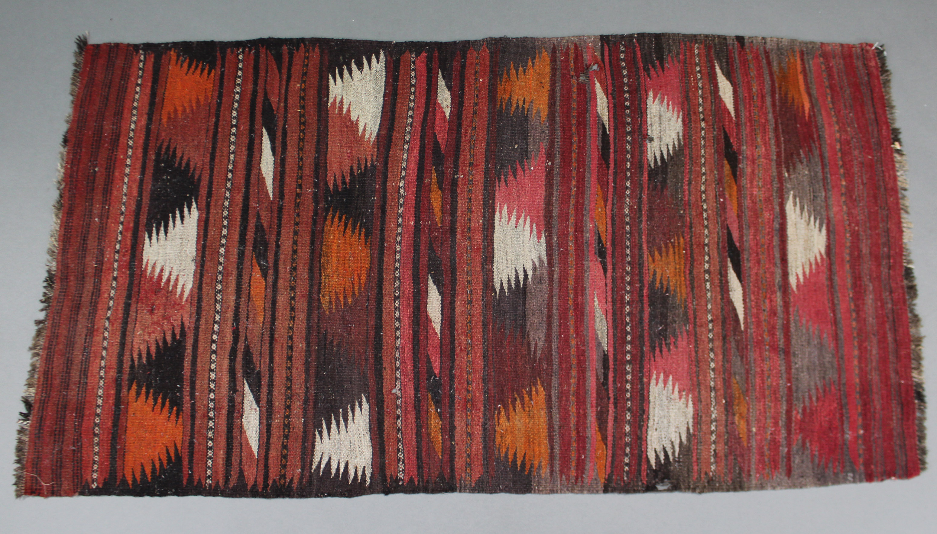 A Kelim rug of crimson ground, 74" x 40" (worn); & a Bokhara small runner, 72" x 25½" (worn).