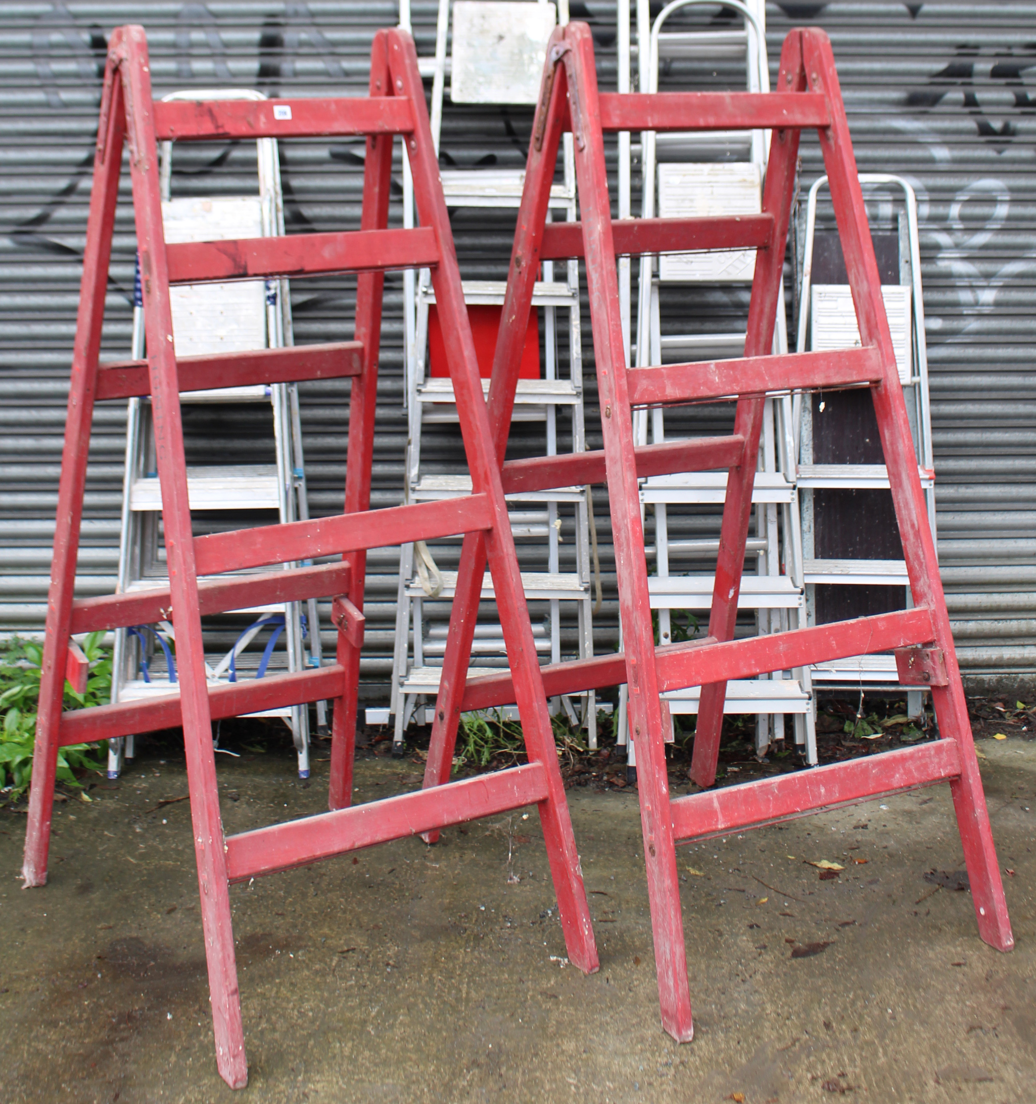 A pair of crimson painted wooden tall decorator’s trestles, 72” high; & seven various aluminium step