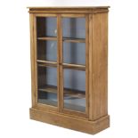 A pine standing bookcase fitted three shelves enclosed by pair of glazed doors, & on plinth base,