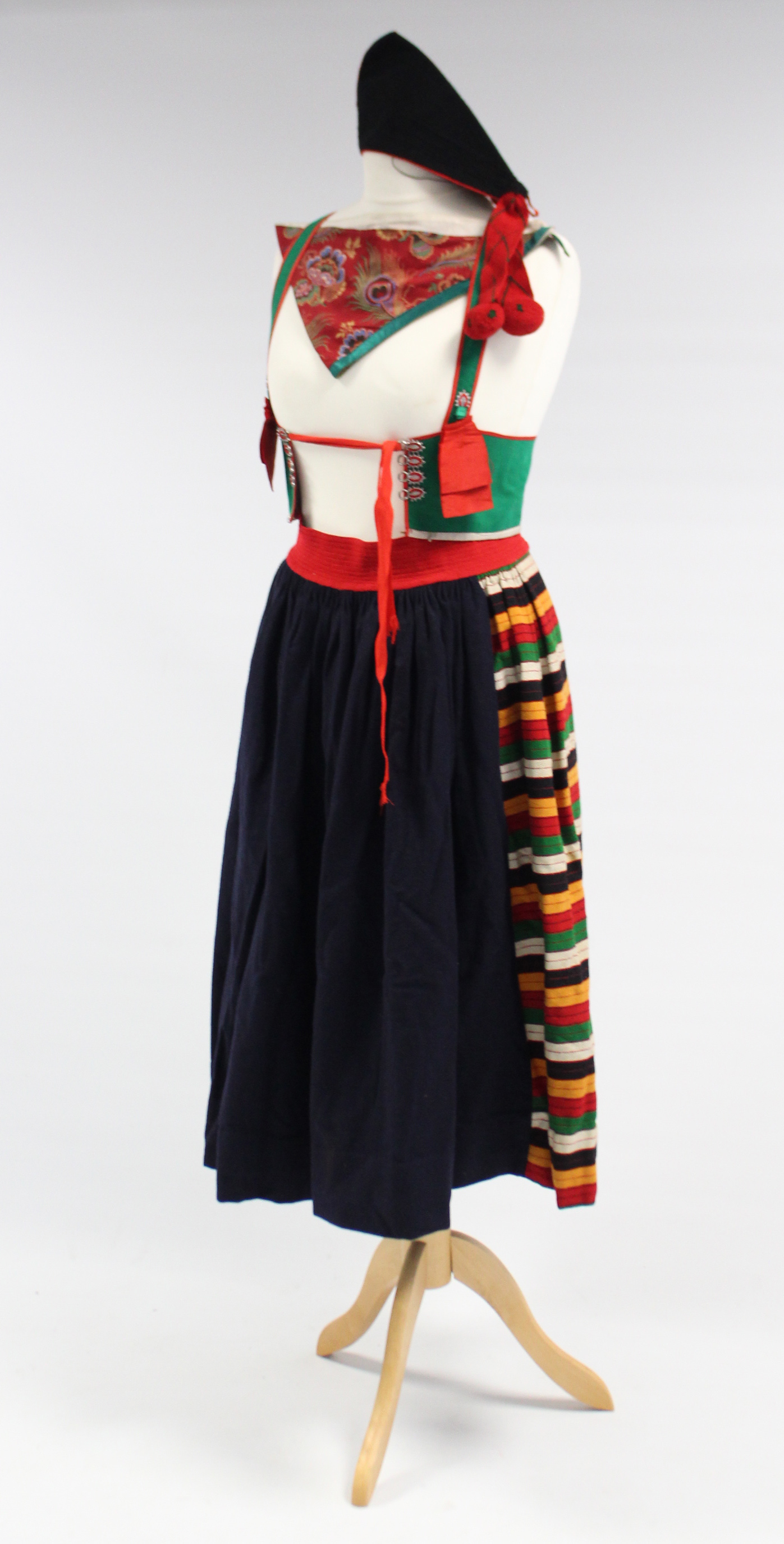 A mid-20th century school girl’s costume comprising a skirt, waistcoat, scarf & a hat.