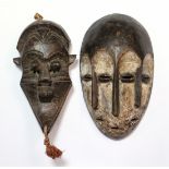 A Lega Bwami three-face mask, 10½”; & another mask with protruding eyes & long pointed chin, 9¼”.