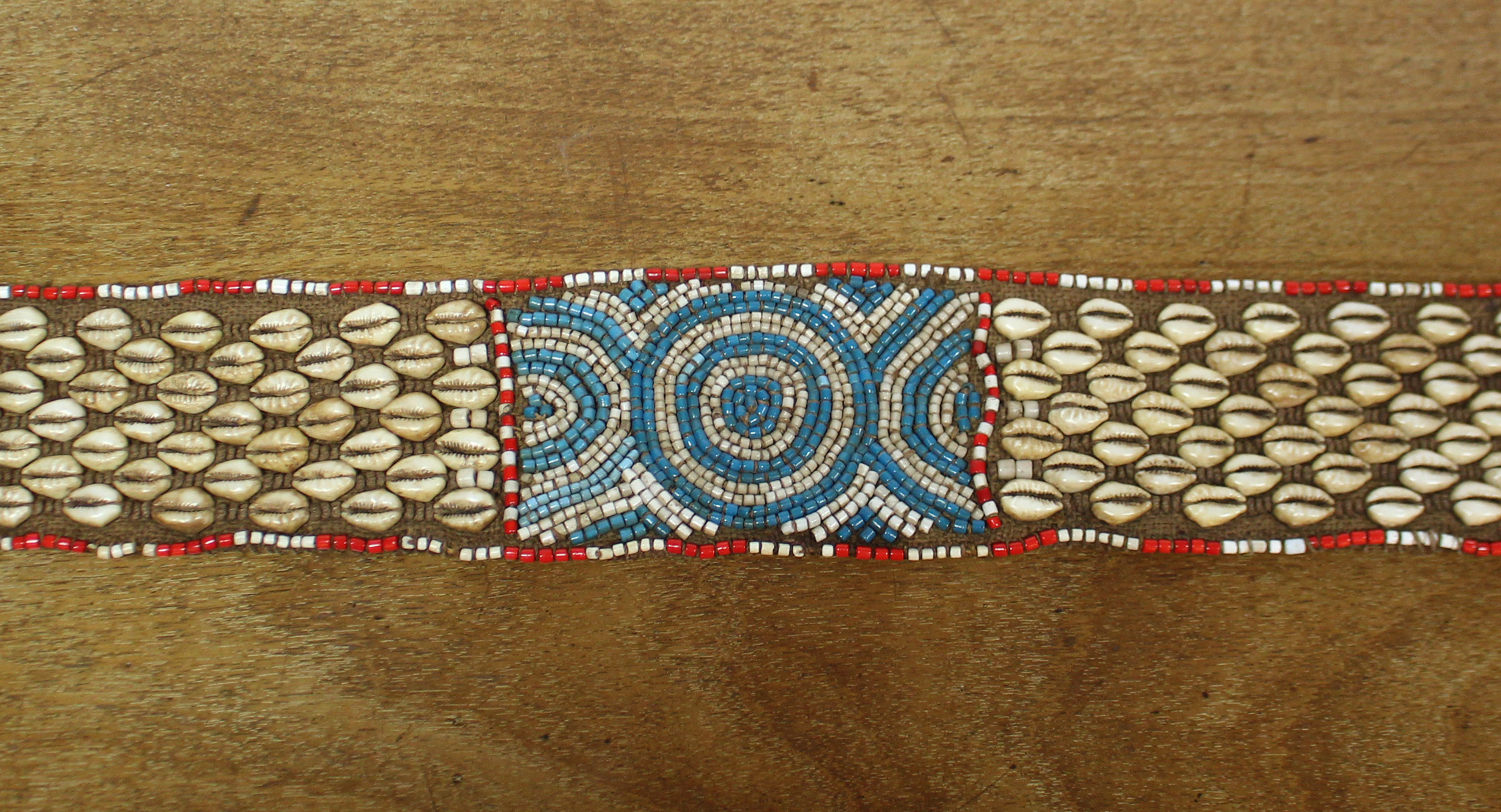 A Kuba woven raffia long belt with diagonal rows of applied cowrie shells either side of a central