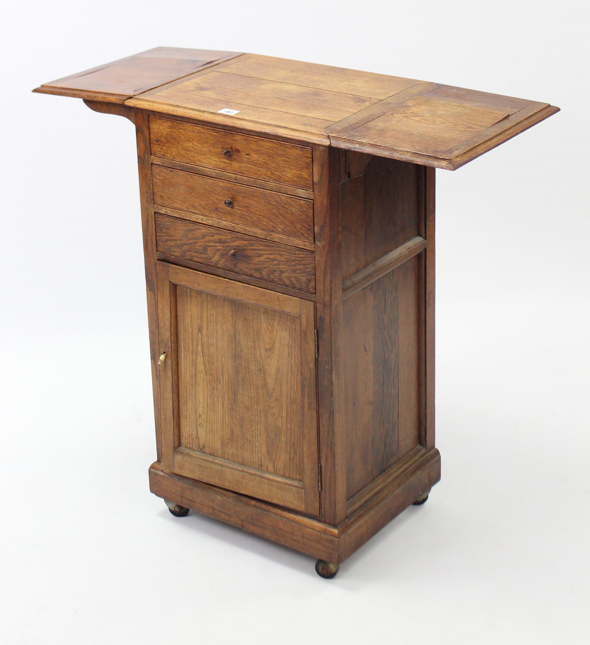An early 20th century oak drop-leaf bedside cabinet fitted three long drawers above cupboard