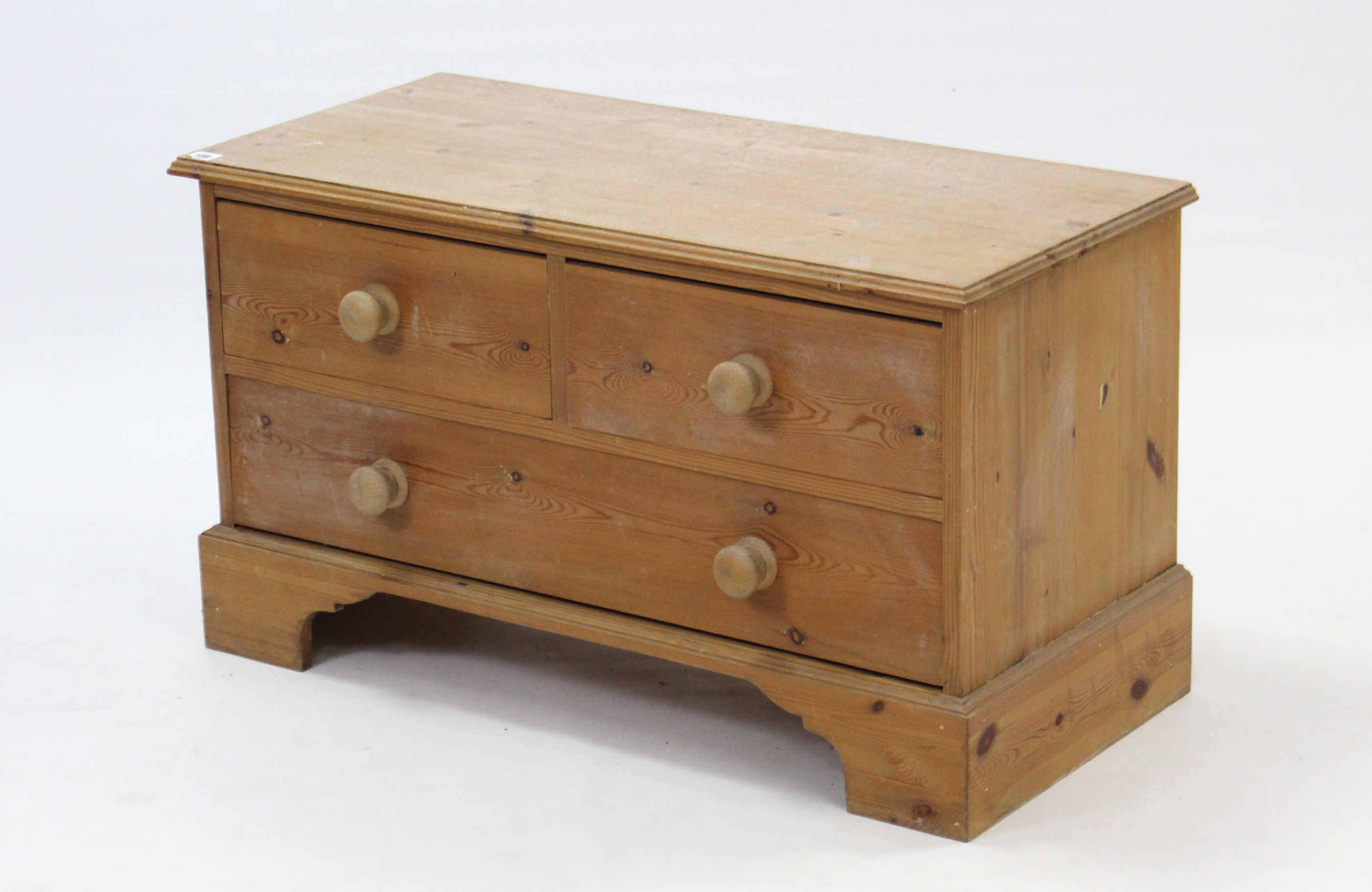 A pine dwarf chest fitted two short & one long drawer with turned knob handles, & on shaped plinth