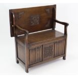 A reproduction oak monk’s bench with fold-over top, hinged lift-seat, & with linen-fold panel front,