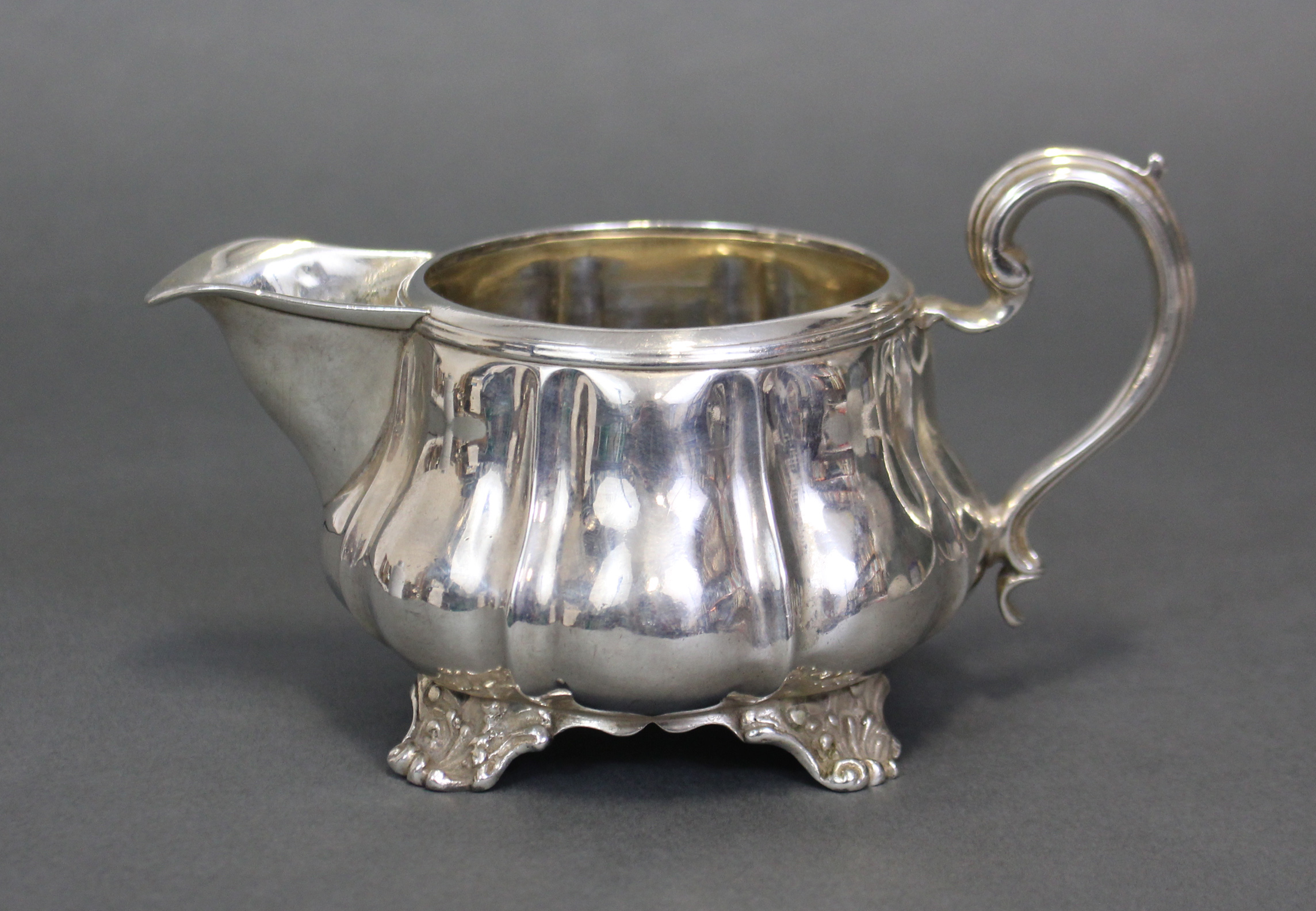A George IV silver melon-shaped milk jug with moulded scroll handle & on four shell-scroll feet;
