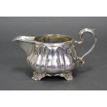 A George IV silver melon-shaped milk jug with moulded scroll handle & on four shell-scroll feet;