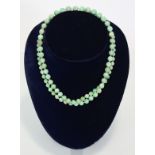 A jade necklace of pale green round graduated beads, the yellow metal pierced oval clasp marked 14K;