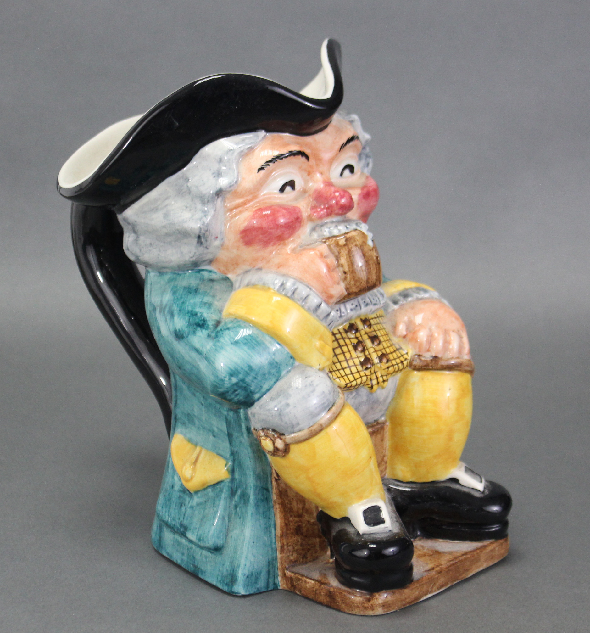 A Clarice Cliff Newport pottery toby jug, the seated Toby with rouge cheeks & nose, clutching a