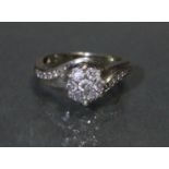 A diamond cluster ring set seven small stones, a row of five further stones to each curved shoulder,