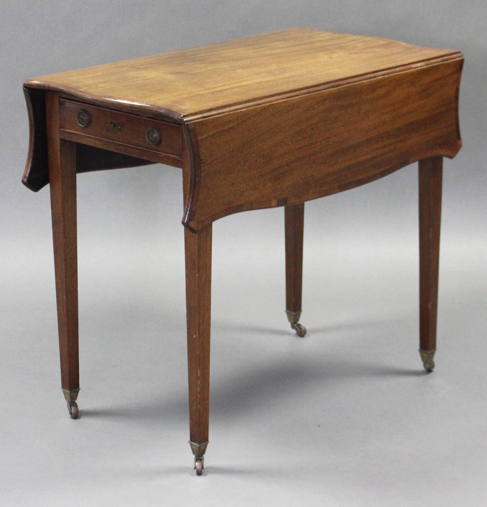 A George III mahogany Pembroke table of serpentine outline, the crossbanded top with canted corners,