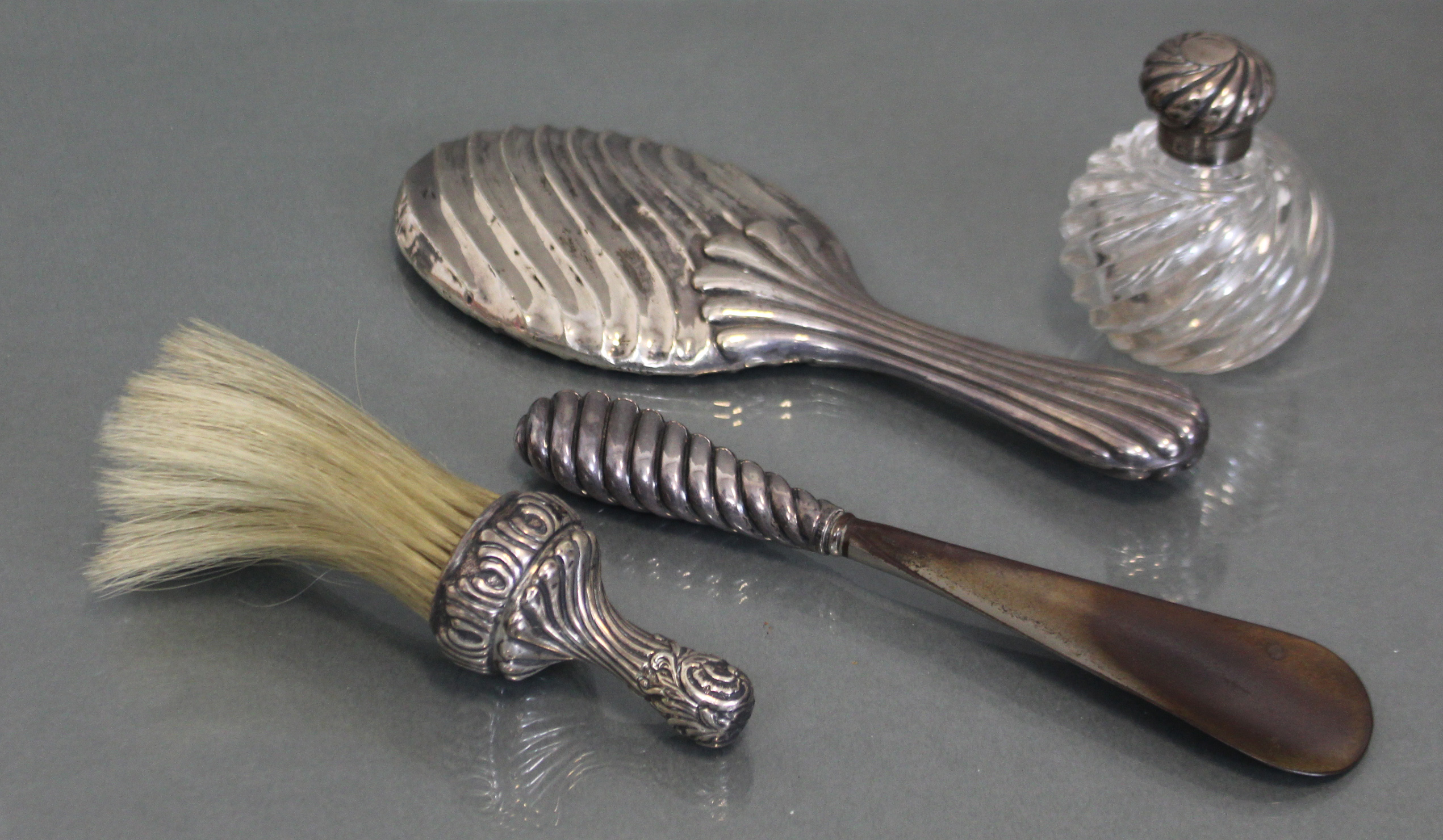 A silver-mounted perfume bottle; a silver-backed hand mirror & similar shoe-horn; & a soft brush