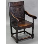 A 17th century JOINED OAK ARMCHAIR, the square panel back with carved floral decoration to the top