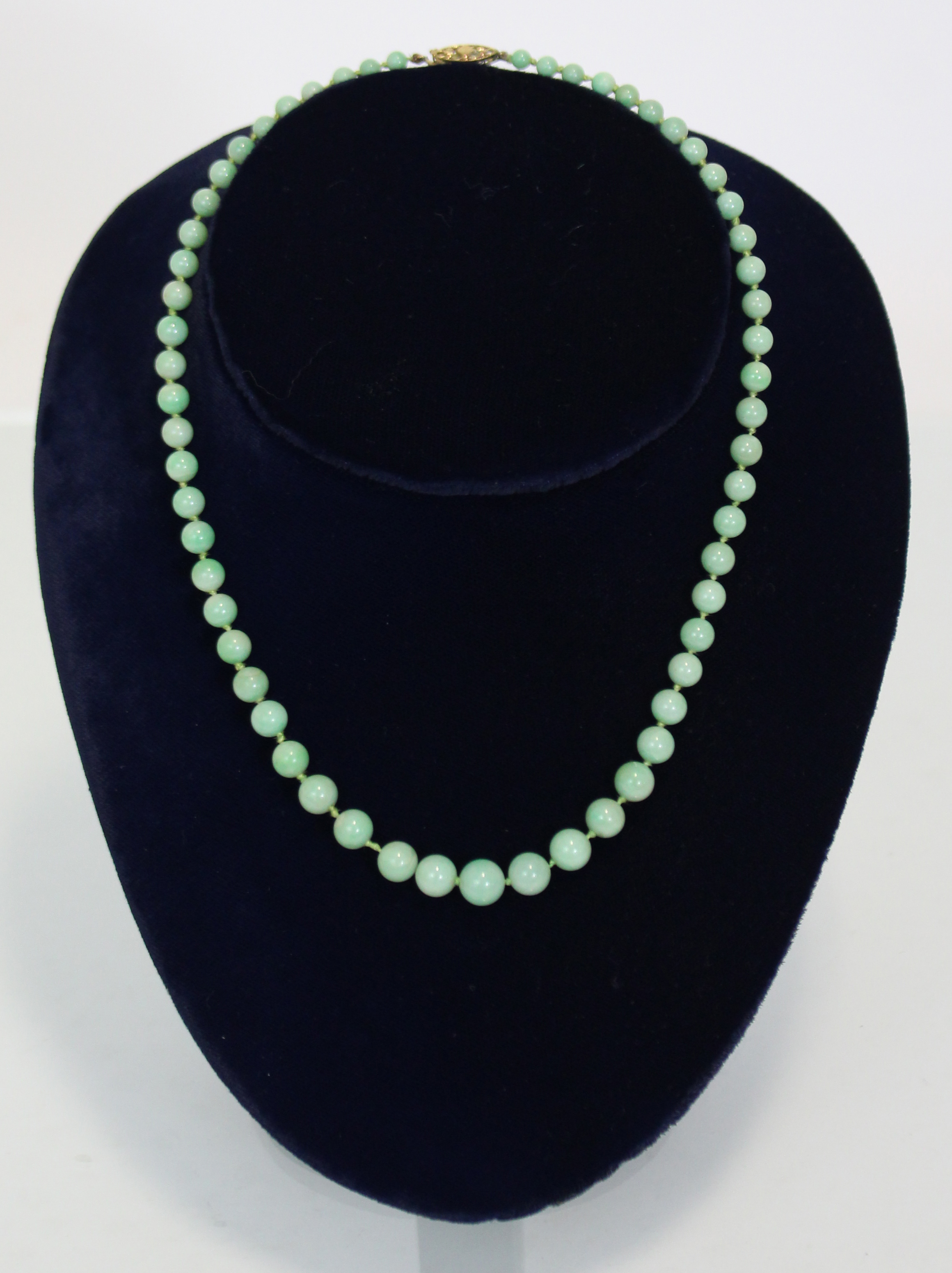 A jade necklace of pale green round graduated beads, the yellow metal pierced oval clasp marked 9ct.