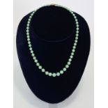 A jade necklace of pale green round graduated beads, the yellow metal pierced oval clasp marked 9ct.