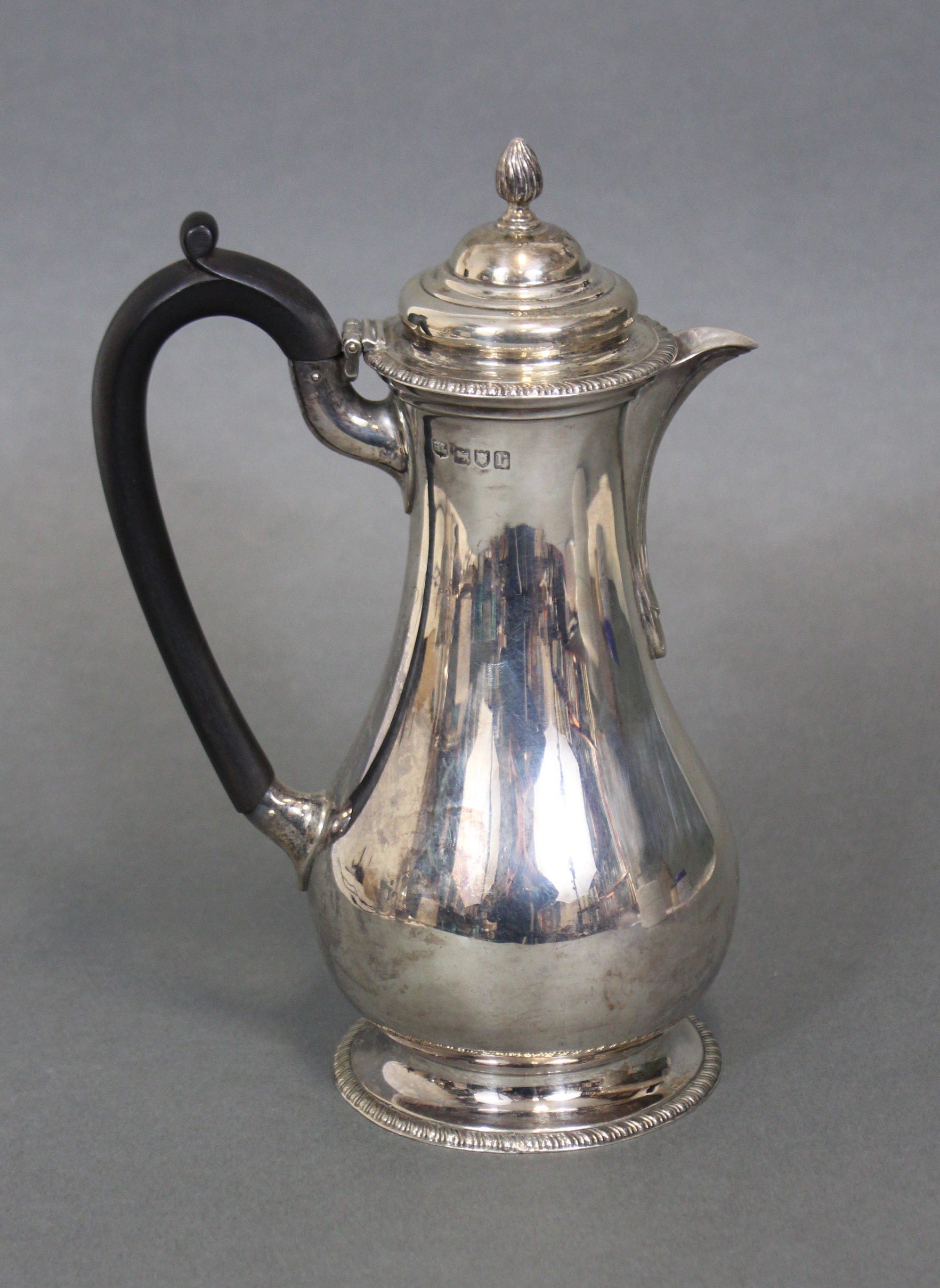 An 18th century-style hot water jug of baluster shape with ebonised scroll handle, hinged lid & on