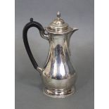 An 18th century-style hot water jug of baluster shape with ebonised scroll handle, hinged lid & on