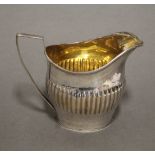 A George III silver oval semi-fluted cream jug with engraved foliate band, reeded angular