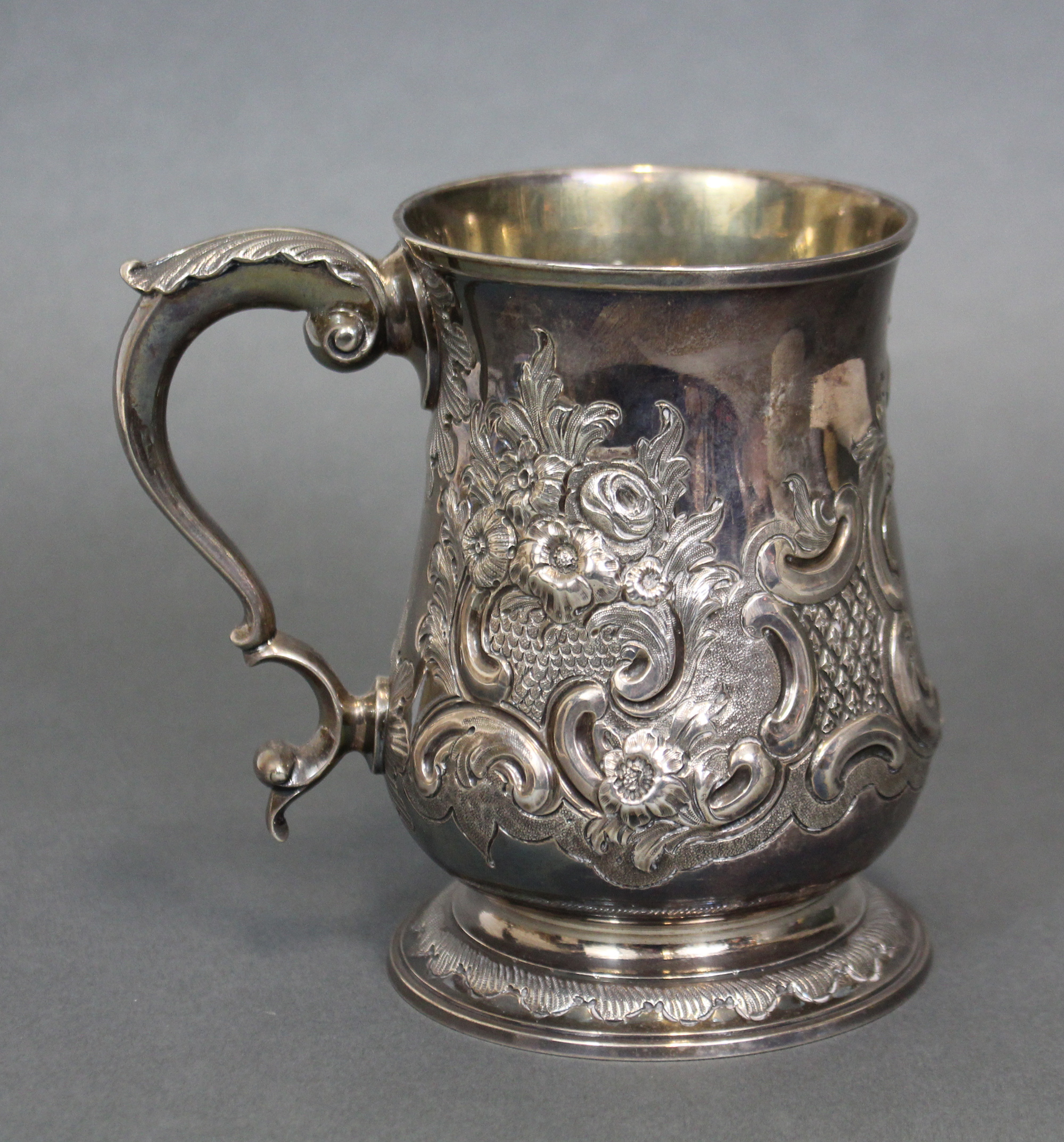 A GEORGE III SILVER TANKARD, the baluster body with embossed decoration of leaf scrolls around a