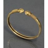 An antique gold torque bangle, the plain body with inwardly-rolled edges & ram’s-head terminals, the