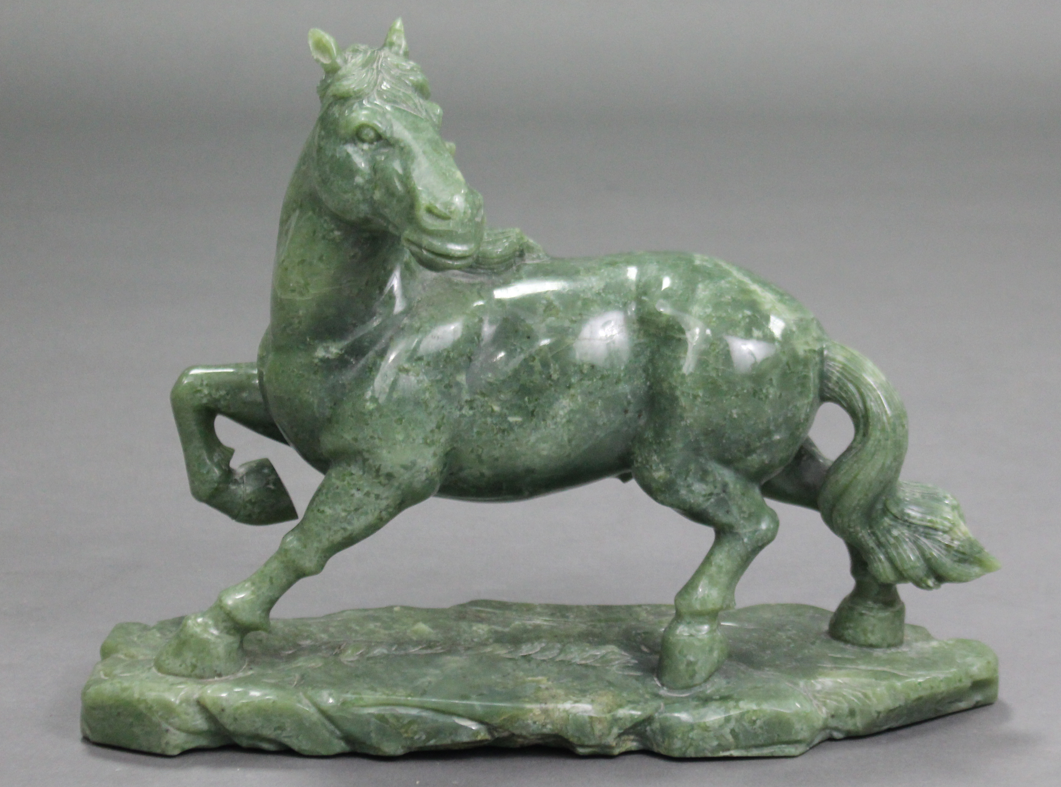 A LARGE CARVED GREEN JADE-ITE MODEL OF A HORSE, its right leg raised & head turned to the left, with