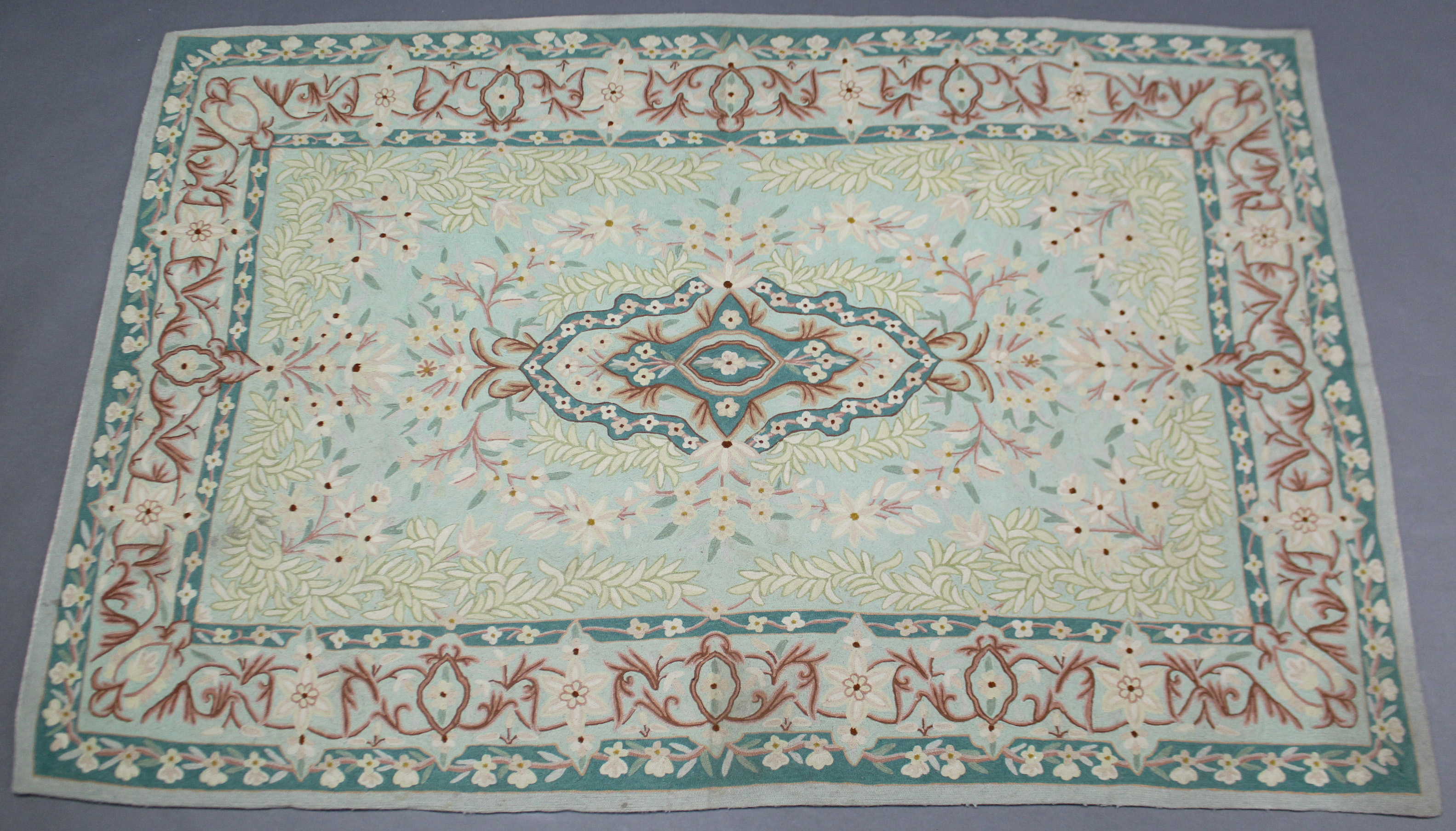 A Kashmiri wool chain rug of pale green ground with a central cartouche surrounded by floral motifs,
