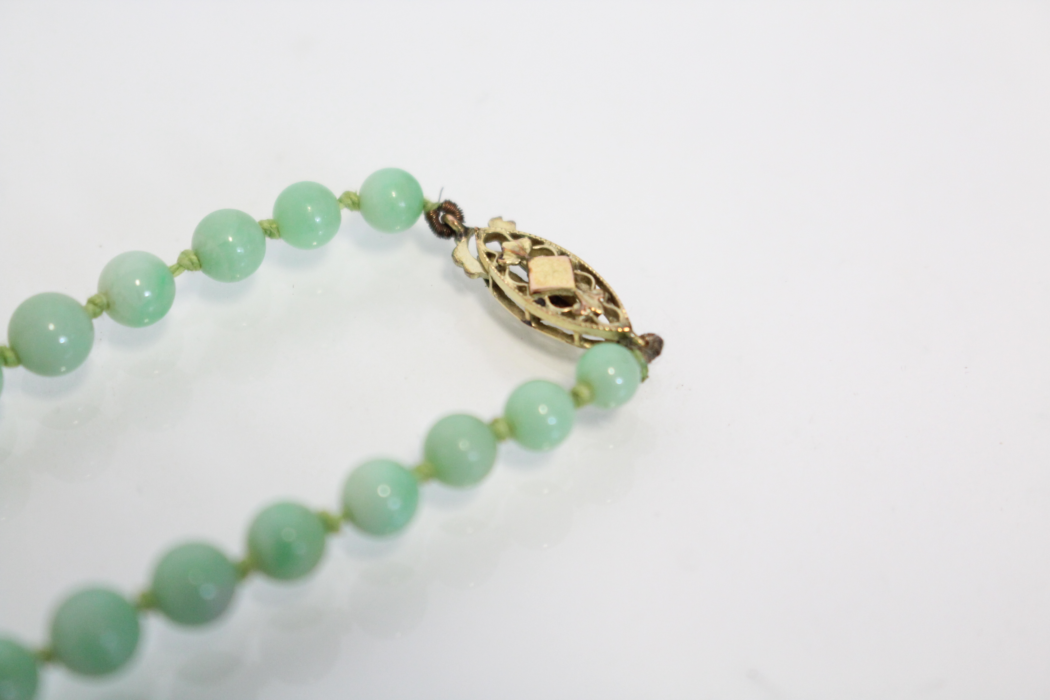 A jade necklace of pale green round graduated beads, the yellow metal pierced oval clasp marked 9ct. - Image 5 of 5