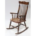 A pine spindle-back rocking chair with hard seat, & on turned supports with spindle stretchers.