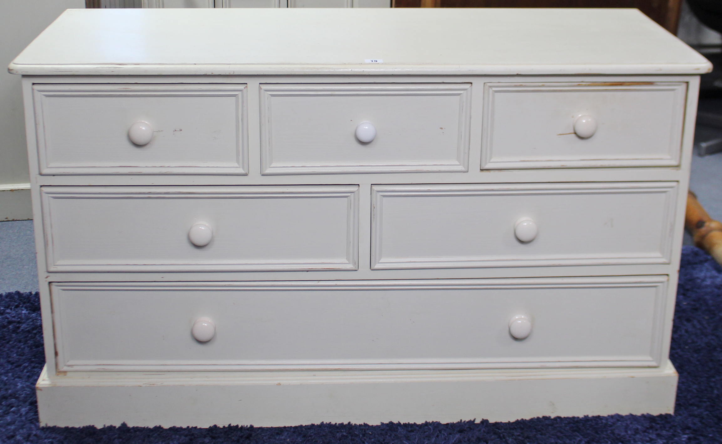 A white painted pine low chest fitted with an arrangement of six drawers with turned knob handles, &