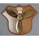 A brass boat propeller stamped “M.C.C. DERE” mounted on walnut shield-shaped wall plaque, bears name