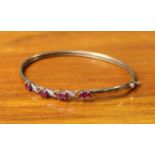 A Shift hinged bangle marked “9K”, set four oval rubies & small diamonds (clasp defective).