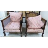 A pair of 1920s carved mahogany framed bergere style chairs with single split cane panels, low,