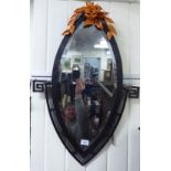 A lozenge shaped bevelled mirror, set in a patinated iron, faux wood frame with Greek key motifs,