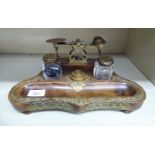An early 20thC mahogany deskstand, incorporating scales and two inkwells with cast brass mounts,