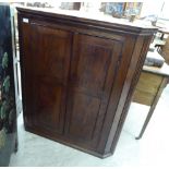 A late 19thC oak hanging corner cupboard with canted flanks, enclosed by a pair of lockable,